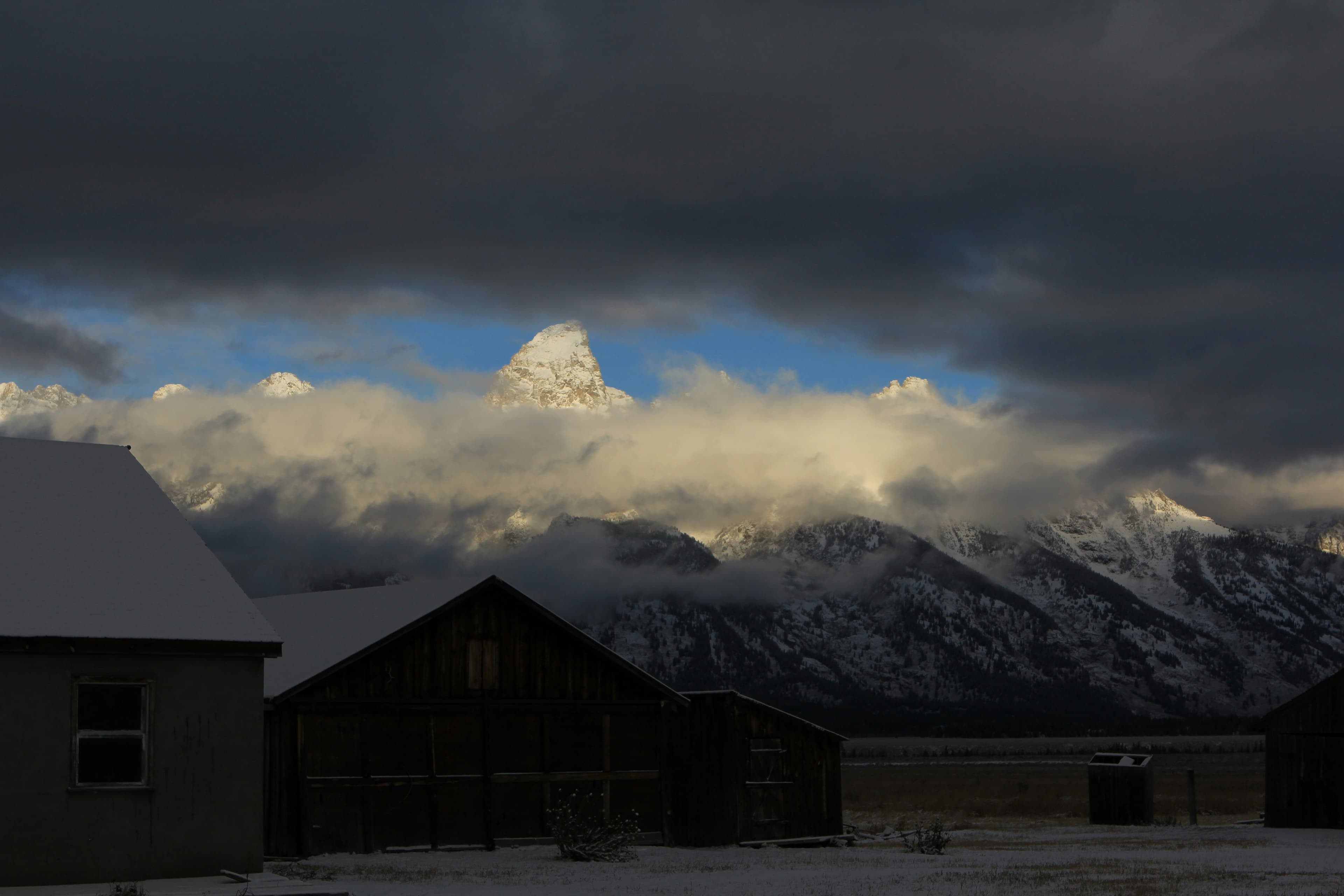 Rustic building with the Teton mountains rising through dramatic clouds behind it